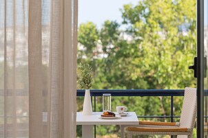 A balcony with a table set for a meal, a wicker chair, a white vase with greenery, and a clear glass bottle.