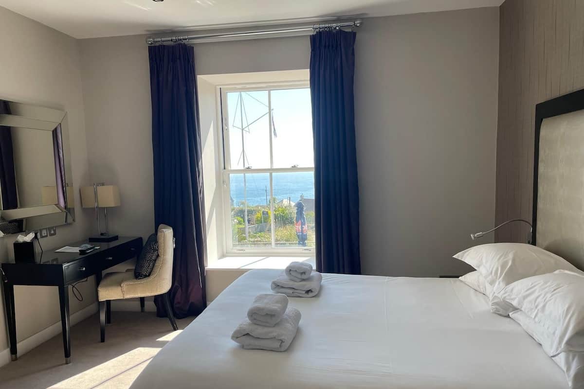 A hotel room with a bed, a desk, a chair, and a large window with curtains.