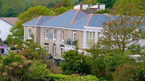A two-story stone house with a sloped roof and a small porch. - The Llawnroc  (St Austell)
