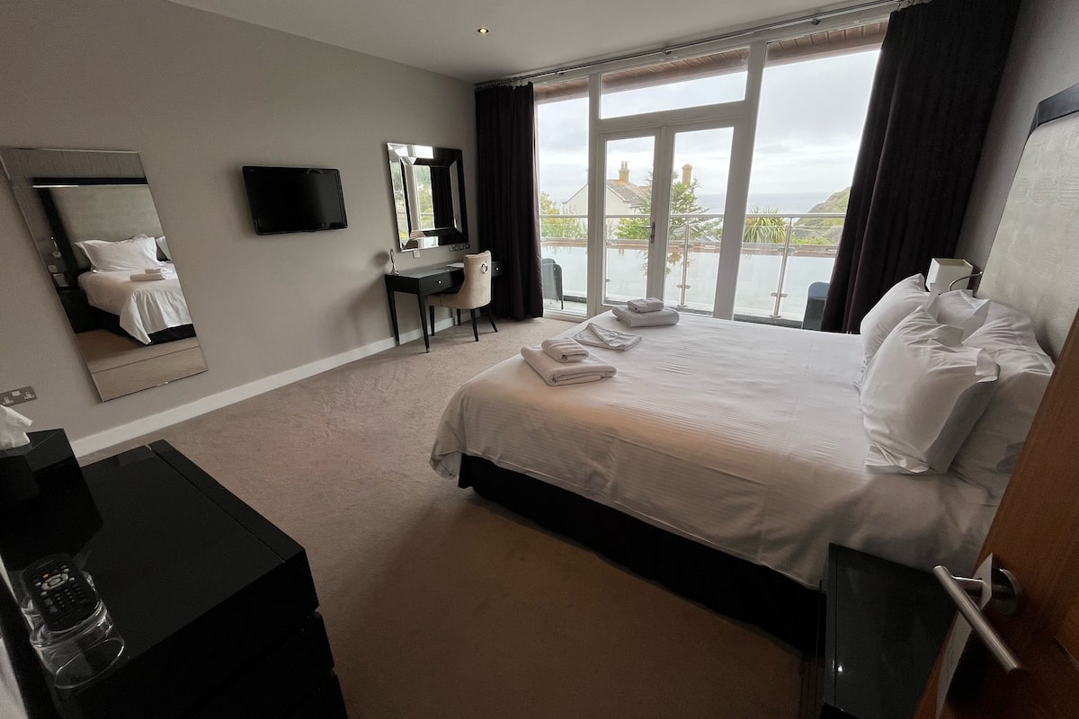 A hotel room with a large bed, a desk, a chair, a TV, and a view of the outdoors.