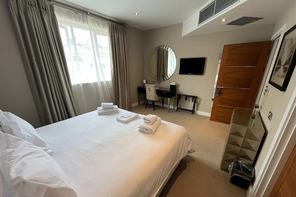A hotel room with a large bed, a desk, a chair, a mirror, and a wardrobe.