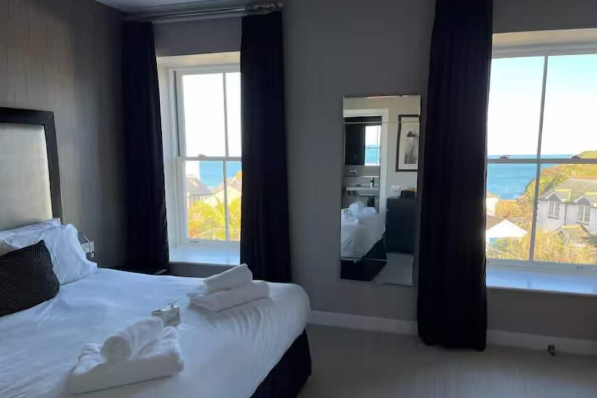 A hotel room with a large bed, a bathroom mirror, and a view of the sea.