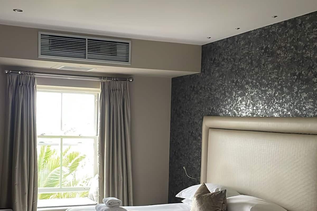 A hotel room with a large bed, a headboard, a bedside table, and a window with curtains.