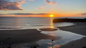 A beach with a sunset, calm water, and a pier. - The Llawnroc  (St Austell)