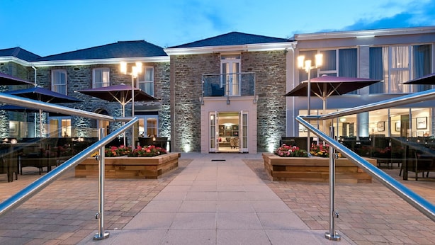 A hotel entrance with a stone facade, outdoor seating, and a staircase leading to the entrance. - The Llawnroc  (St Austell)