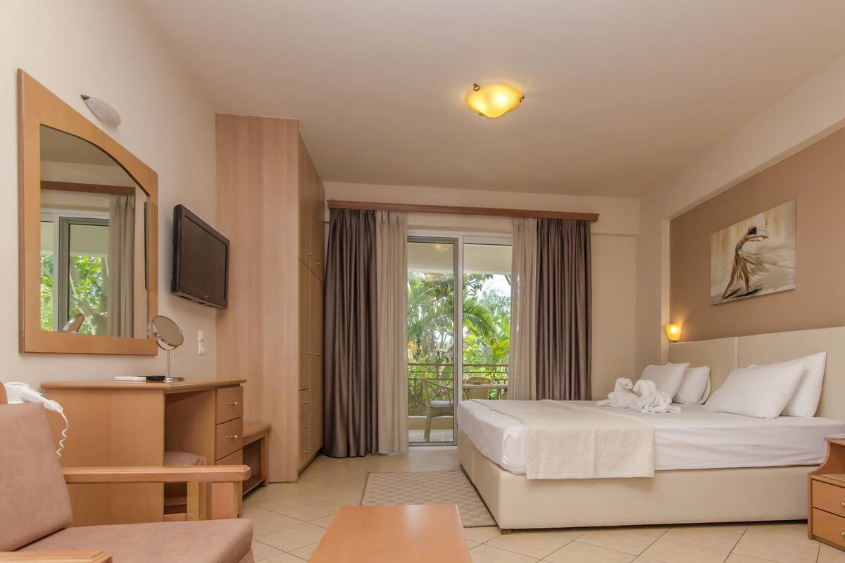 A hotel room with a bed, a desk, a chair, a TV, and a balcony with curtains.