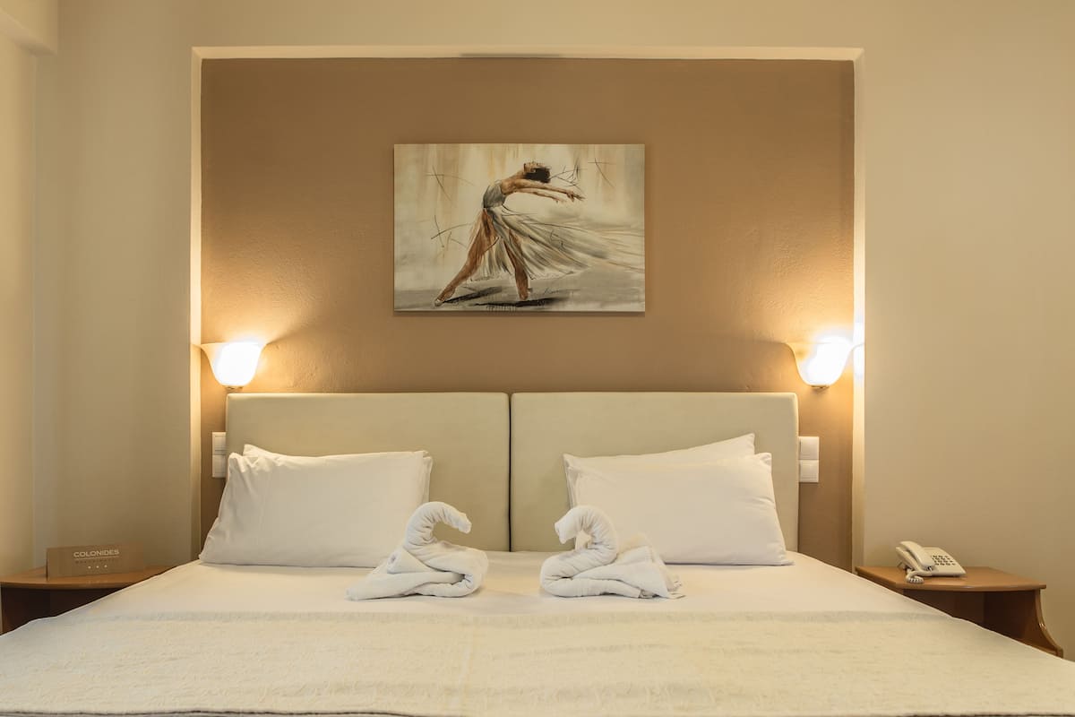 A hotel room with a large bed, two pillows, a painting on the wall, and two bedside lamps.