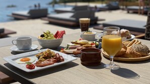 A breakfast table with various dishes, a glass of orange juice, and a view of the sea. - Colonides Beach Hotel (Pylos-Nestoras)