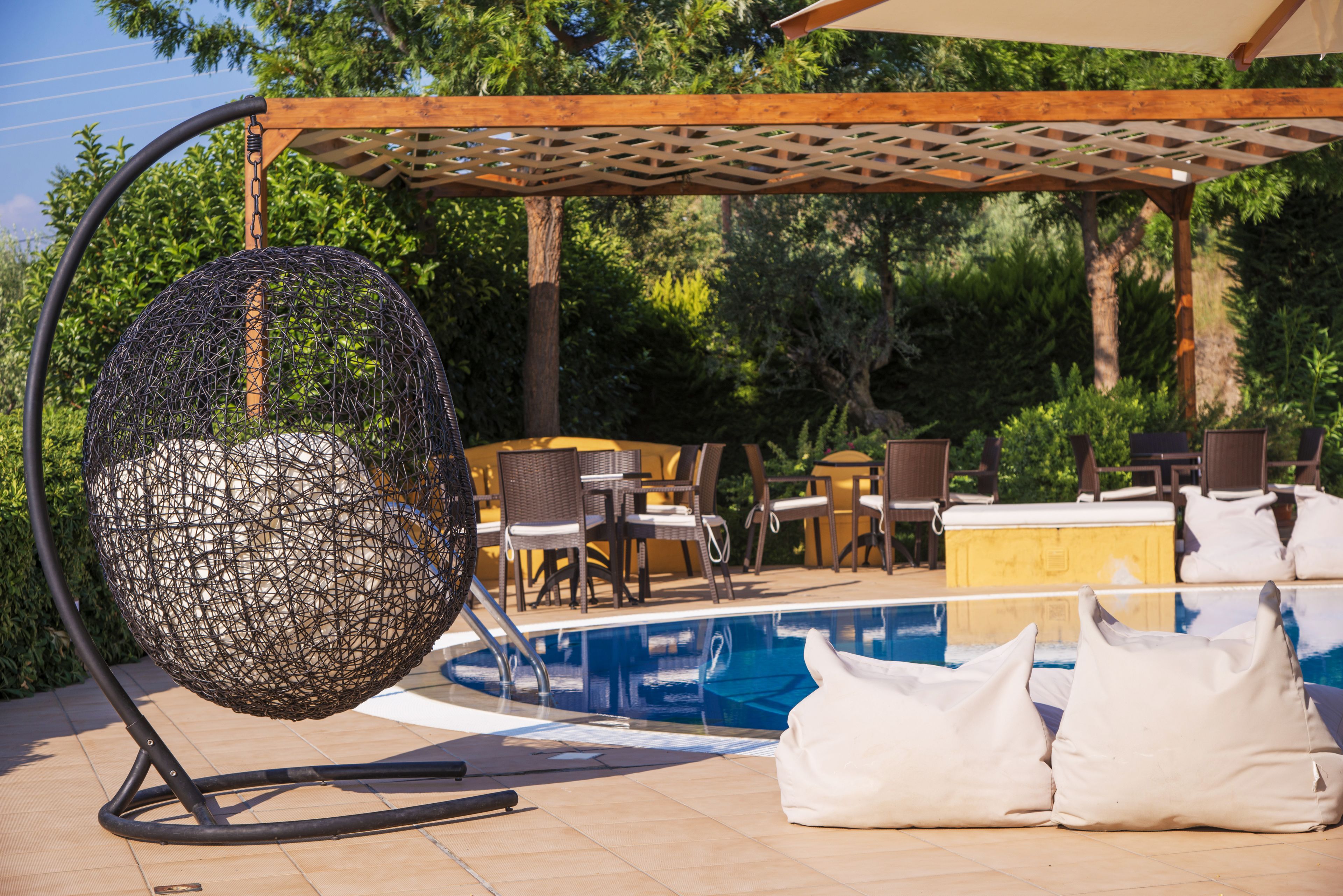 Zona piscina con una sedia a dondolo, mobili da esterno e un pergolato.