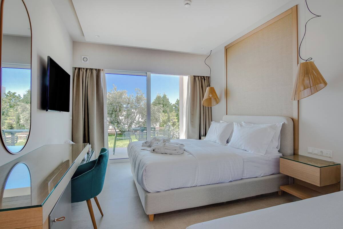 A modern bedroom with a large bed, a glass desk, a TV, and a view of the outdoors.