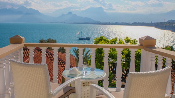 Un balcón con mesa y sillas que da a vistas de la costa, con un barco a lo lejos.