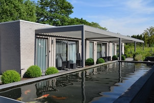 Un edificio moderno con una zona de estar cubierta al aire libre y un estanque de carpas.