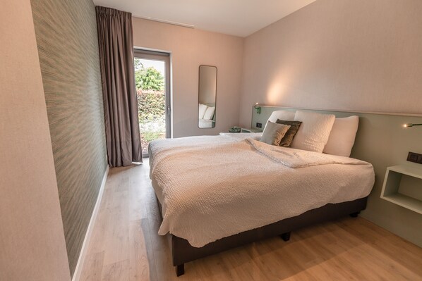 Un dormitorio moderno con una cama grande, una mesita de noche, un espejo y vistas al exterior.