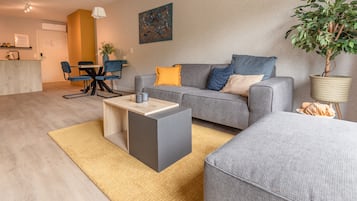 Un salon moderne avec un canapé gris, une petite table basse et un coin repas comprenant une table et des chaises.