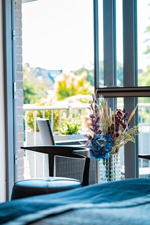 A modern room with a large window, a dining table, and a vase of flowers. - Abalona Hotel & Apartments (Dendermonde)