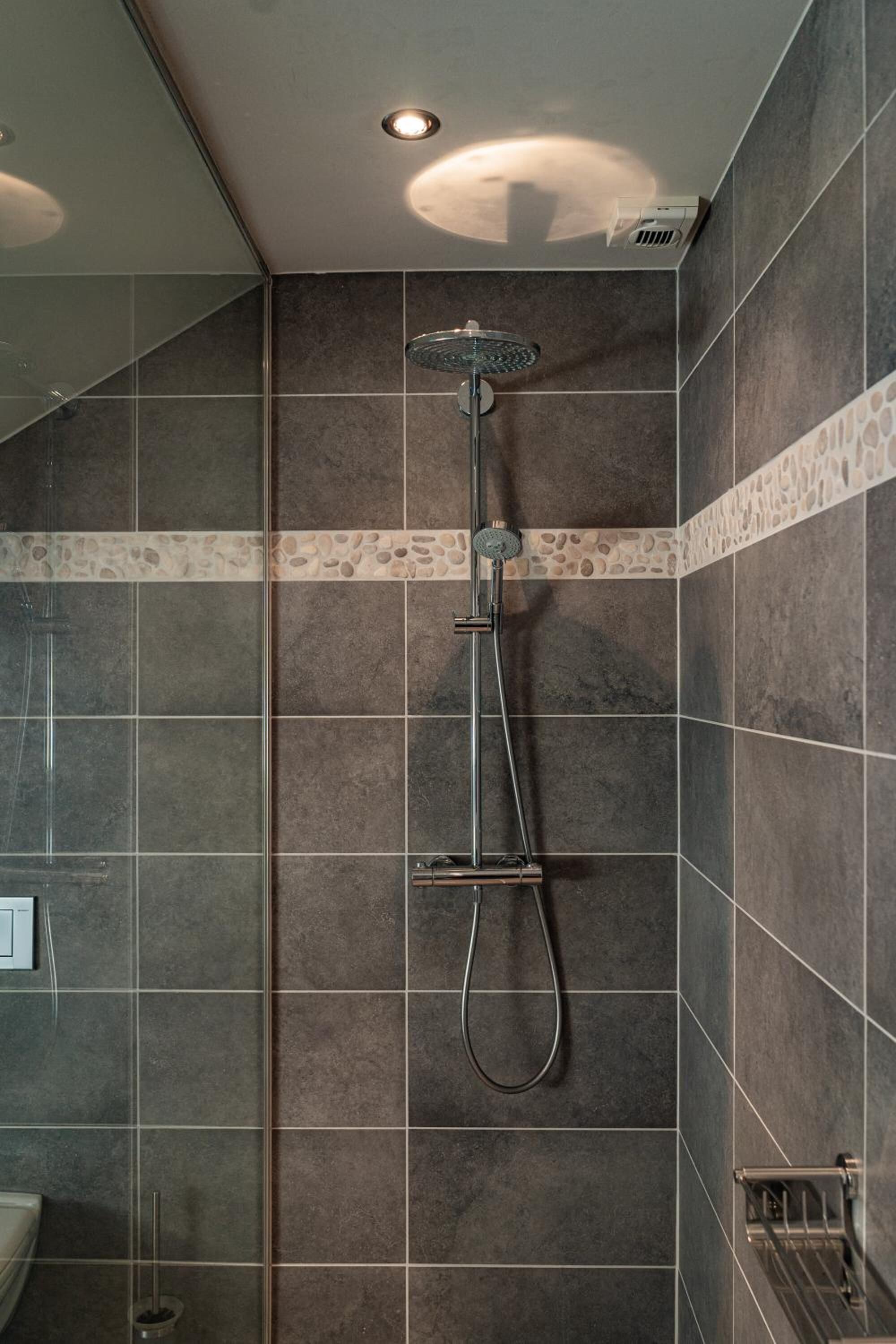 Een douche met een handdouche en een bedieningspaneel aan de muur.