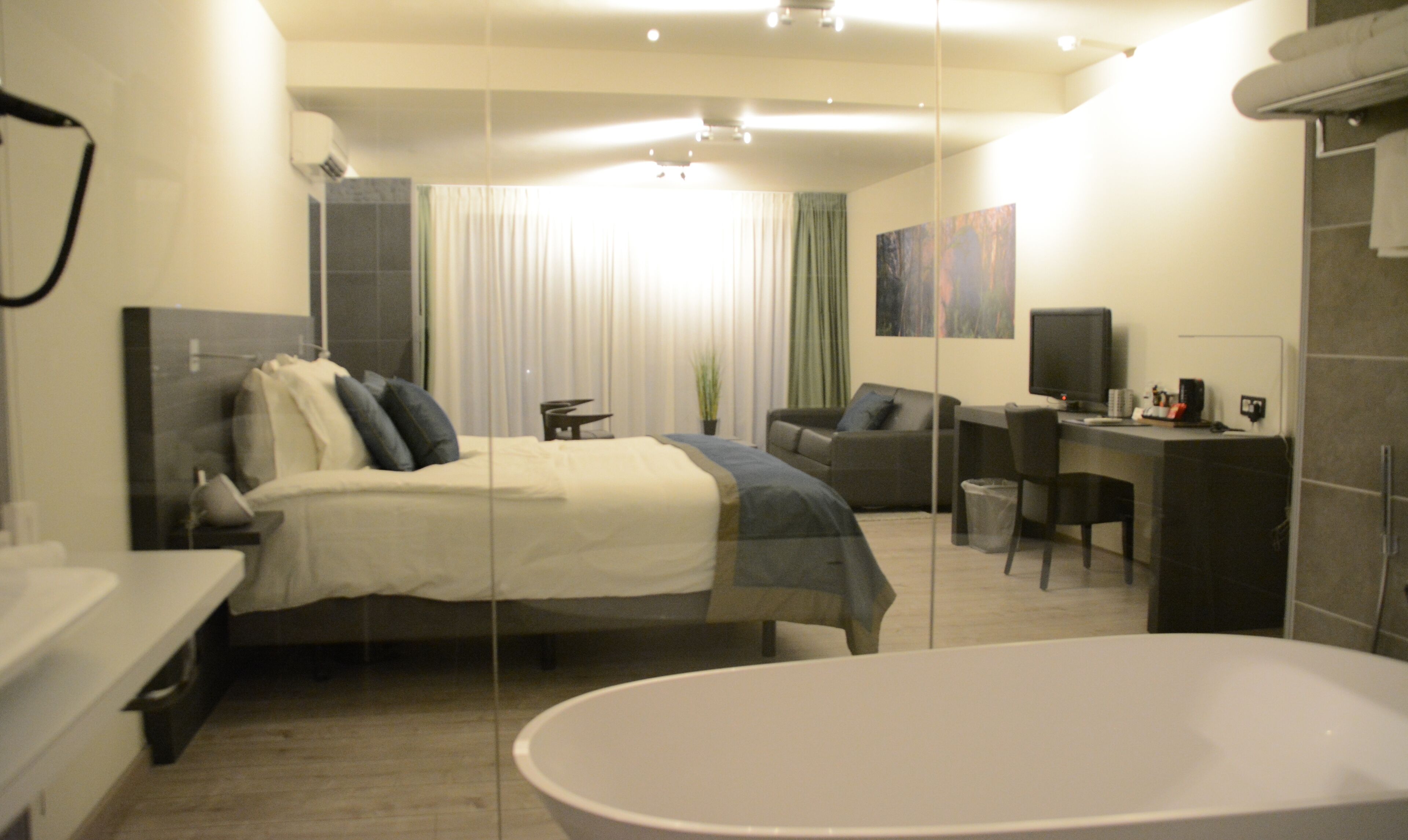 Quarto de hotel moderno com uma cama grande, uma escrivaninha, computador e área de banheiro separada.