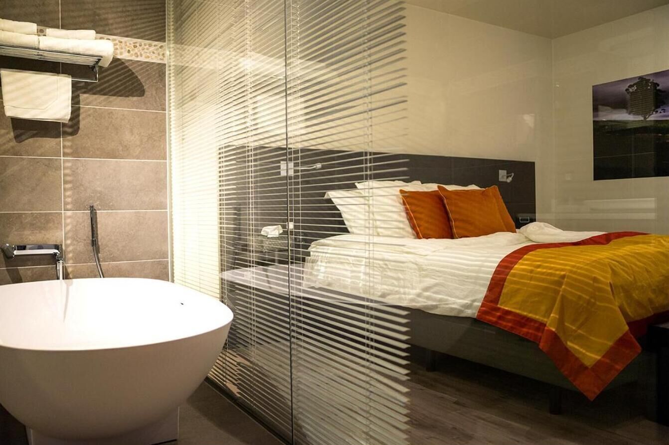 A modern bedroom with a large bed, a glass partition, and a standalone bathtub.