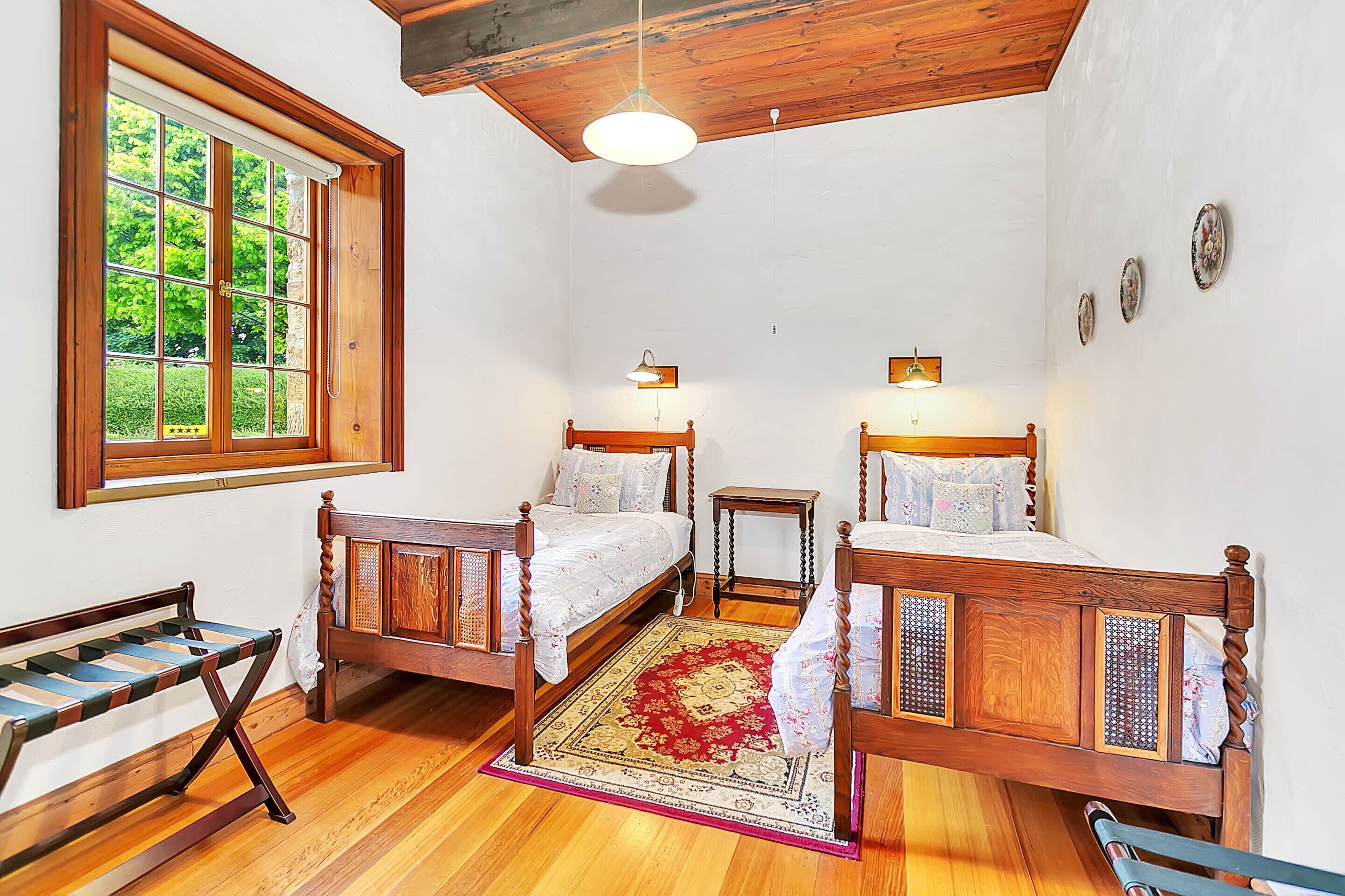 A bedroom with two wooden beds, a bench, a window, and a ceiling light.