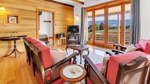 Una sala de estar acogedora con paredes y muebles de madera, un televisor y un amplio ventanal corredero que da a una vista panorámica al exterior.