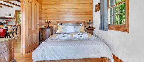 A wooden-paneled bedroom with a bed, bedside tables, and a window with curtains.
