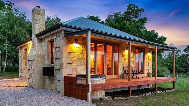 Una casa de piedra con un porche cubierto, chimenea y mobiliario exterior.