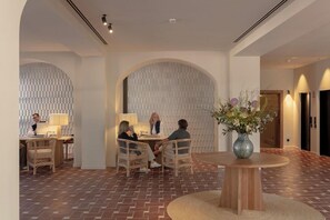 A modern interior with a herringbone floor, a round wooden table with a vase, and a person working at a desk. - Hotel Rovira (Tossa de Mar)