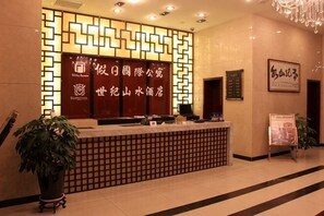 A reception desk with a patterned backdrop, a potted plant, and a signboard.