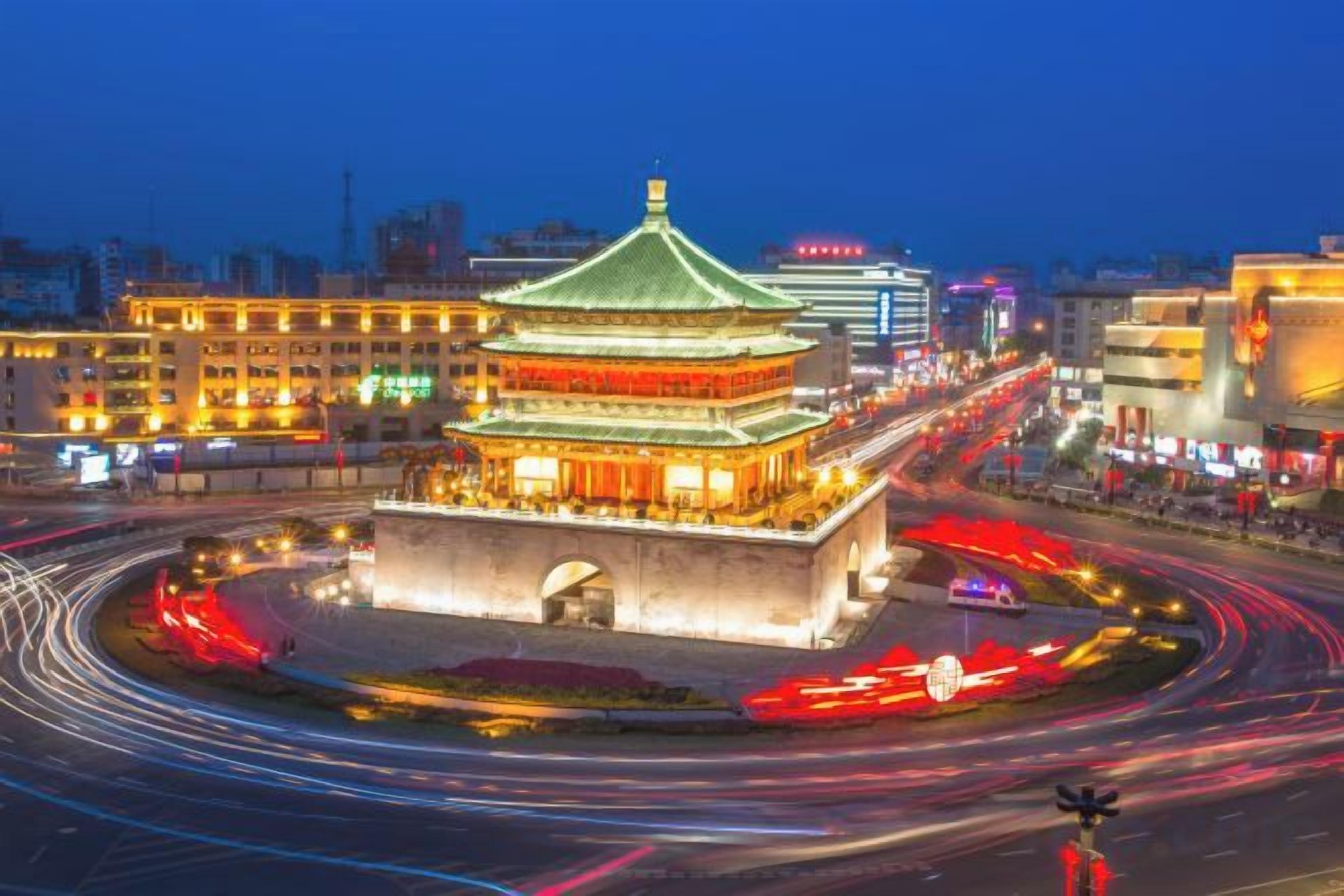 A traditional building with a green roof, surrounded by a roundabout with light trails indicating traffic.