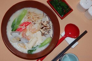 A bowl of soup with various ingredients, a red spoon, chopsticks, and a small dish of greens. - Century Landscape Hotel (Xi'an)