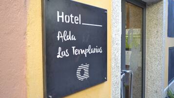 Señal del Hotel Alda Los Templiers, colocada sobre una pared amarilla.