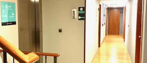 Un pasillo de hotel con una escalera de madera, un ascensor y una zona de recepción.