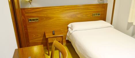 A hotel room with a wooden headboard, a single bed, a wooden nightstand with a remote control, and a chair.