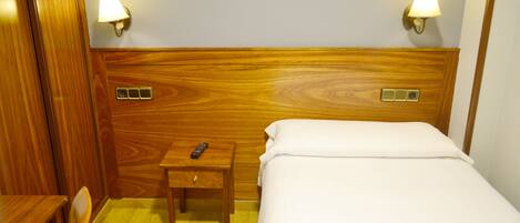 Una habitación de hotel con cabecera de madera, dos lámparas de noche, una mesita de noche con un control remoto y una cama con ropa de cama blanca.
