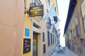A narrow street with a hotel sign, outdoor seating, and a flag. - Hotel Los Templarios (Ponferrada)