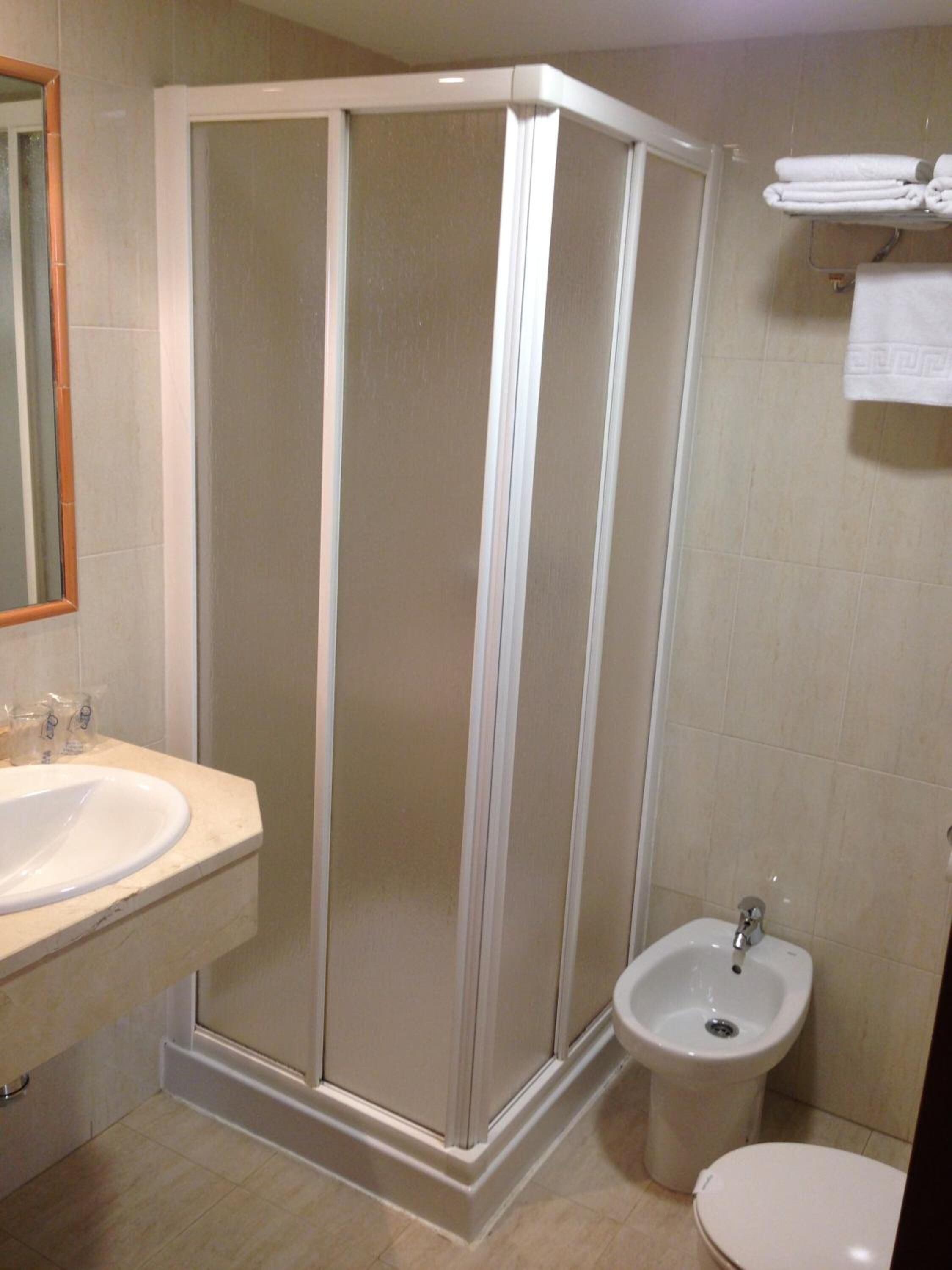 A bathroom with a shower enclosure, a sink, a bidet, and a toilet.