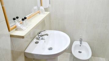 A bathroom with a white sink, a bidet, and a shelf with toiletries.