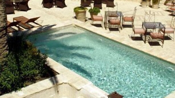 A pool area with lounge chairs and a stone building with a cross on top. - La Hospederia Del Monasterio (Osuna)