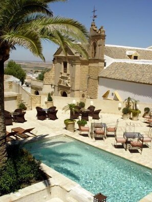 A pool area with lounge chairs and a stone building with a cross on top.