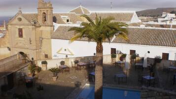 A courtyard with a pool, palm trees, and traditional architecture including a church and tiled roofs.