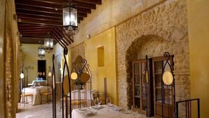 A dining area with stone walls, wooden beams, and hanging lanterns. Tables are set with plates and wine glasses. - La Hospederia Del Monasterio (Osuna)