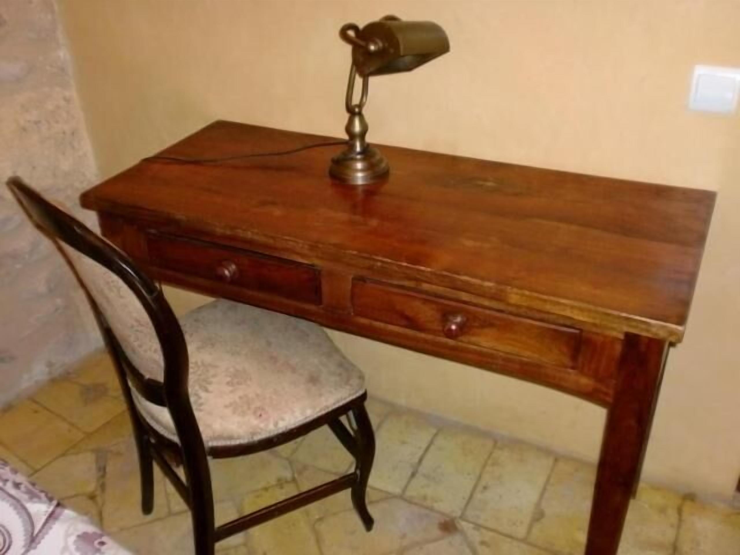 A wooden desk with a chair, a lamp, and a drawer.