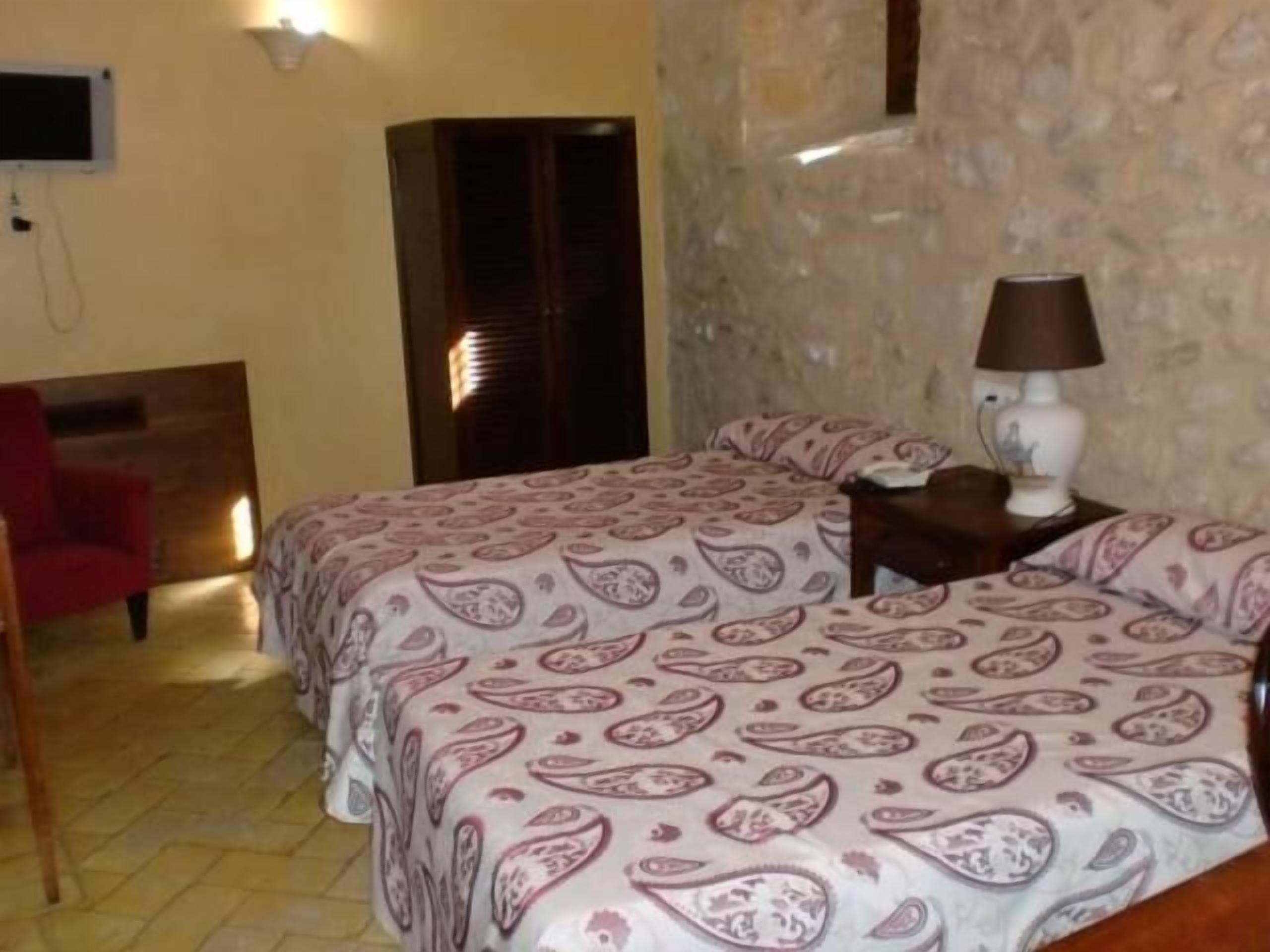 Un dormitorio con cama, mesita de noche, lámpara, silla y pared de piedra.