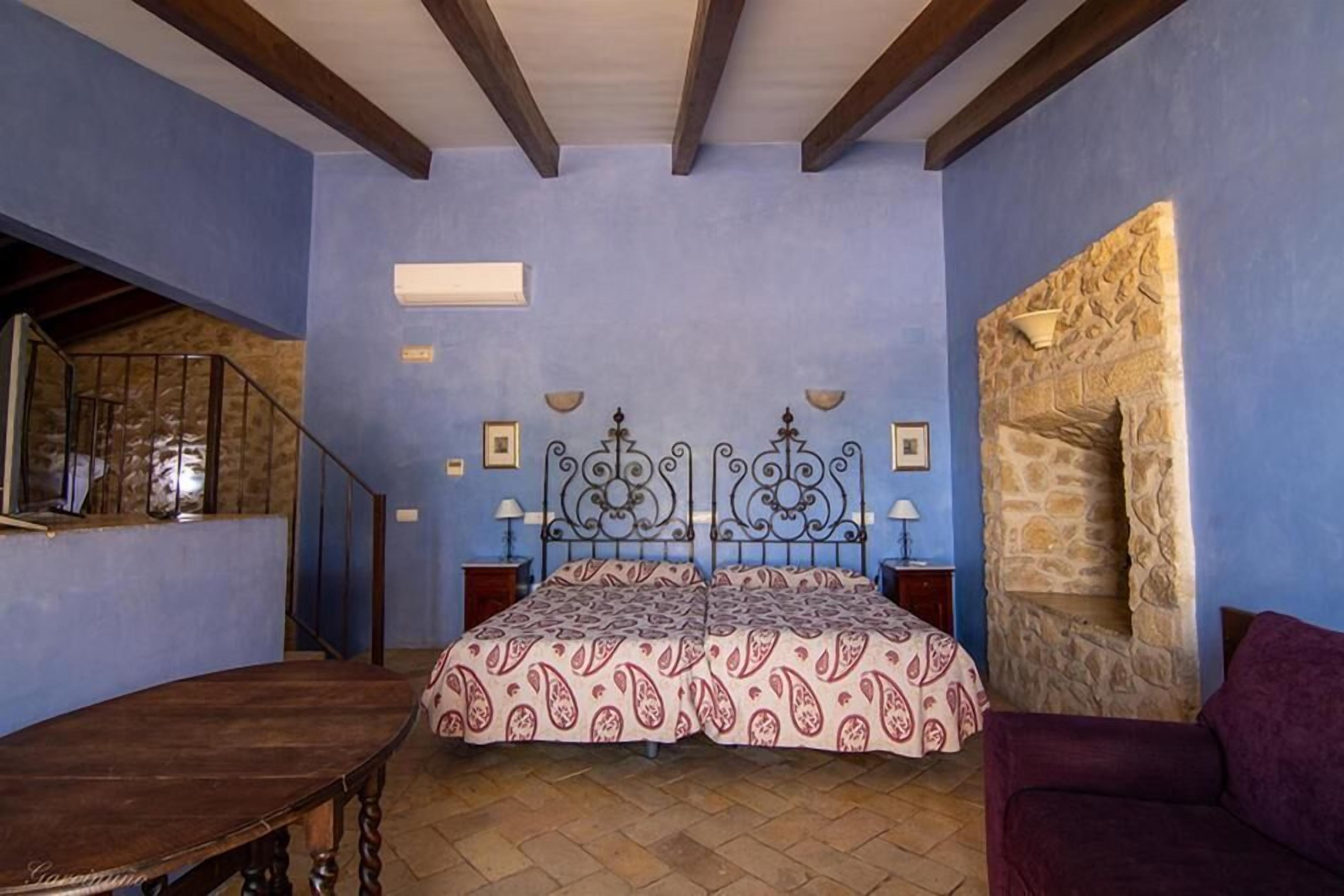 Een slaapkamer met een bed, een houten tafel, een paarse bank en een stenen muur.