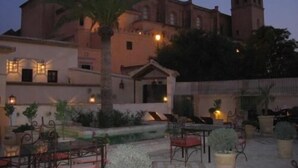 A courtyard with outdoor seating, a palm tree, and a building with a tower. - La Hospederia Del Monasterio (Osuna)