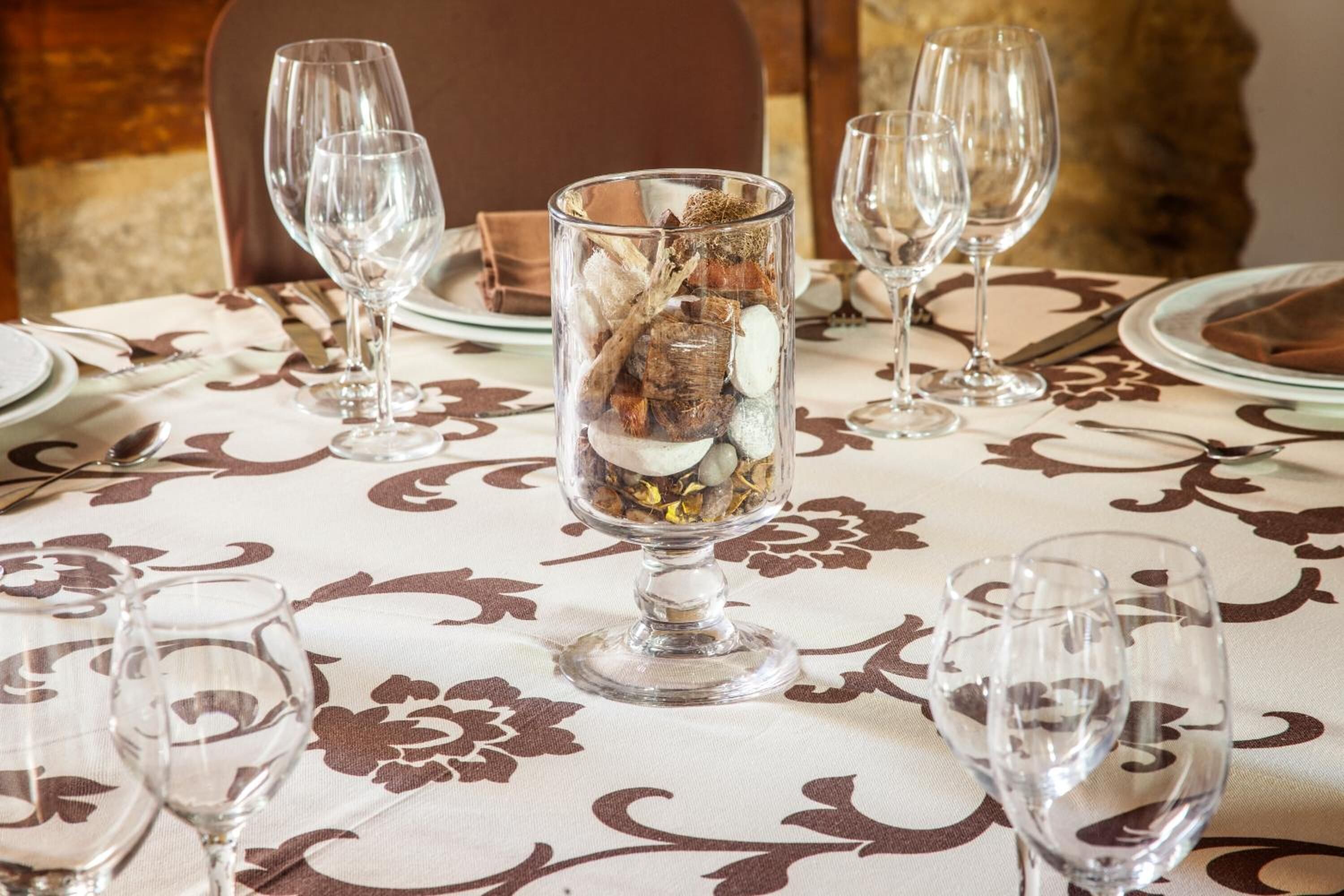 Una mesa de comedor dispuesta con cristalería transparente y un centro de mesa con flores secas y ramas.
