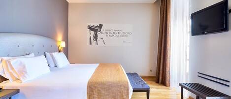 Una habitación de hotel moderna con una cama grande, un banco, un televisor de pantalla plana y una frase motivadora en la pared.