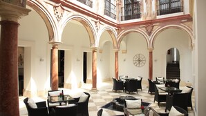 Un patio amplio con varias zonas de estar, incluyendo mesas y sillas, rodeado de arcos y columnas.