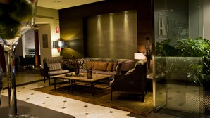 Un moderno vestíbulo de hotel con un sofá, sillones, una mesa de centro y un separador de vidrio con plantas.