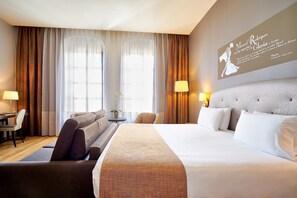 A hotel room with a large bed, a sofa, a desk, and a lamp. There is a window with curtains and a wall with a framed picture. - Hotel Eurostars Patios de Córdoba (Córdoba)